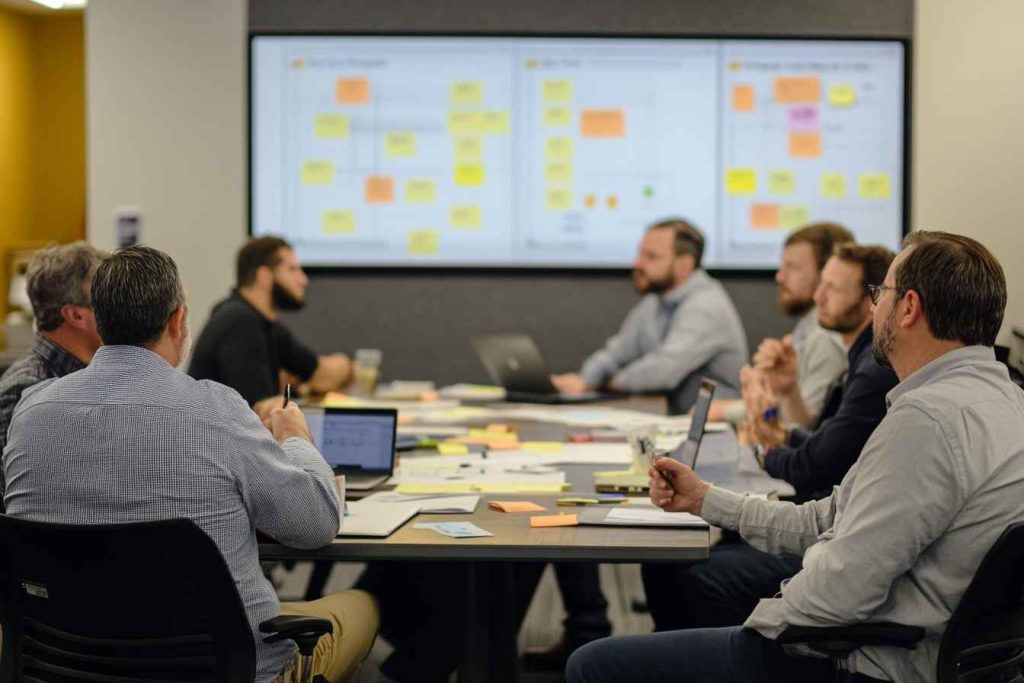 hybrid-negotiation-task-delegation A male team lead negotiating task priorities with hybrid team members in a collaborative meeting.